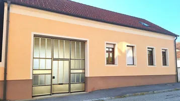 Fassade eines Gebäudes mit großer Garagentür und kleinen Fenstern in warmen Farbtönen.