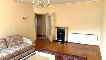 Gemütliches Wohnzimmer mit Parkettboden, Kronleuchter und einem traditionellen Gasofen.