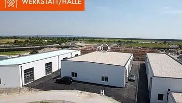Moderne weiße Hallengebäude mit Flachdächern und Parkplätzen in einer ländlichen Umgebung mit Baustellen im Hintergrund.