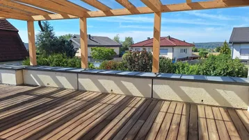 Geräumige Dachterrasse mit Holzbelag, Pergola und weitem Blick über die Umgebung.