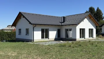 Neubau-Einfamilienhaus mit weißer Fassade und dunklem Satteldach auf einem großen Grundstück.