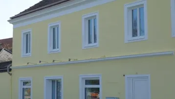 Gut erhaltene Fassade eines Altbaus in hellem Gelb mit weißen Fensterrahmen und Dach.