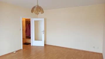 Heller, leerer Raum mit Laminatboden und einer Tür zu einem angrenzenden Bereich.