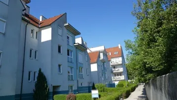 Mehrere Wohngebäude mit hellblauer Fassade und roten Dächern unter blauem Himmel.