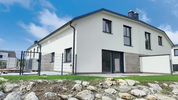 Moderne Doppelhaushälfte mit weißer Fassade und dunklem Dach unter blauem Himmel.