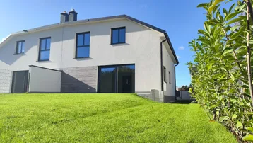 Modernes Reihenhaus mit weißer Fassade und gepflegtem Rasen unter blauem Himmel.