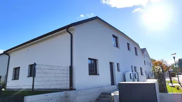 Moderne Doppelhaushälfte mit weißer Fassade, gepflastertem Eingangsbereich und blauem Himmel.