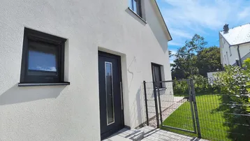 Eingangsbereich eines modernen Neubaus mit gepflastertem Zugang und kleiner Grünfläche.