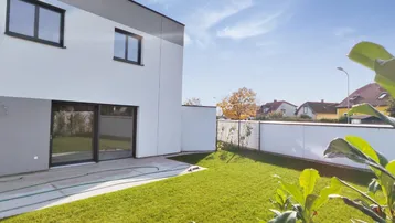 Moderner Neubau mit weißer Fassade, großem Garten und Zugang zur Terrasse.