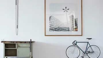 Minimalistischer Raum mit Werkbank, Fahrrad und großem Kunstwerk an der weißen Wand, sehr hell.