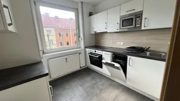 Helle Küche mit weißen Schränken, integrierten Geräten und Blick auf die Stadt.