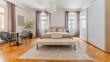 Helles Schlafzimmer mit Parkettboden, großem Bett, Einbauschränken und einem kleinen Essbereich.