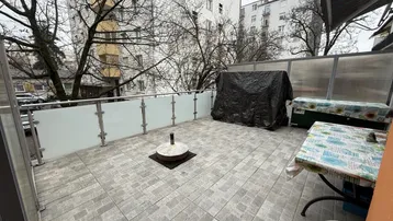 Geräumige geflieste Terrasse mit Glasgeländer und Blick auf umliegende Gebäude und Bäume.