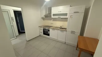 Helle Einbauküche mit weißen Schränken, Kochfeld und Kühlschrank, praktisch gestaltet.