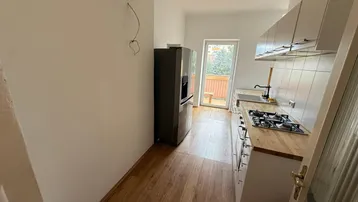 Moderne Küche mit weißen Schränken, Holzarbeitsplatte und Zugang zu einem Balkon.