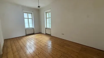Helles, leeres Zimmer mit Holzdielenboden und zwei Fenstern, bereit zur individuellen Gestaltung.