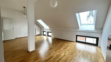 Lichtdurchfluteter Dachgeschossraum mit Parkettboden und Blick auf eine Kirchturmspitze.