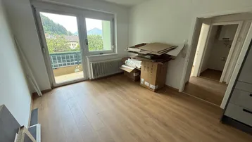 Geräumiger, heller Raum mit Balkonzugang, Laminatboden und Blick auf die Berge.