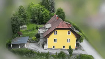 Luftaufnahme eines gelben Hauses mit rotem Dach, umgeben von viel Grün und Bäumen.