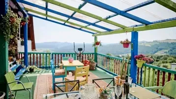 Bunte überdachte Terrasse mit Esstisch und Stühlen, bietet einen weiten Blick auf die Landschaft.