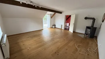 Geräumiges Wohnzimmer mit Holzboden, freiliegendem Holzbalken, Kaminofen und Zugang zum Außenbereich.
