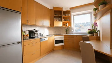 Helle Küche mit Holzfronten, integrierten Geräten und einem Essbereich am Fenster.