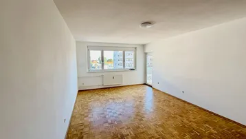 Helles Zimmer mit Fischgrätparkett, weißen Wänden und Zugang zu einem Balkon oder einer Loggia.