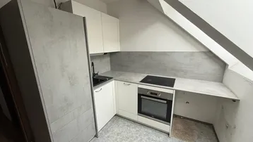 Moderne Einbauküche im Dachgeschoss mit Schrägdach, integriertem Backofen und Induktionskochfeld.