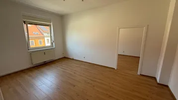 Geräumiges Zimmer mit Laminatboden und weiß gestrichenen Wänden, ideal als Wohn- oder Schlafzimmer.