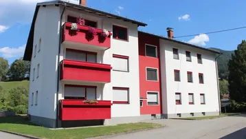 Mehrfamilienhaus mit weißer und roter Fassade sowie Balkonen unter blauem Himmel.