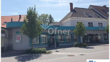 Außenansicht eines Geschäftsgebäudes mit blauer Fassade und Parkplätzen davor unter blauem Himmel.