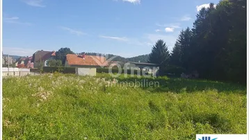 Weitläufiges grünes Grundstück mit Blick auf umliegende Häuser und bewaldete Hügel unter blauem Himmel.