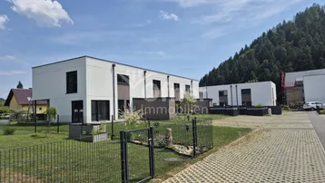 Moderne Reihenhäuser mit wei ßer Fassade und Blick auf bewaldete Hügel unter blauem Himmel.