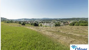 Weitläufige Landschaft mit grünen Feldern und Blick auf eine Siedlung in der Ferne.