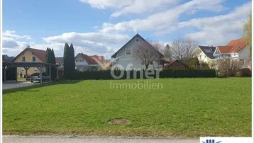 Weitläufige Rasenfläche mit Blick auf eine Wohnsiedlung und einen Carport.