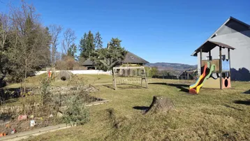Großer Gartenbereich mit Spielplatz, Rutsche und Schaukel unter blauem Himmel.