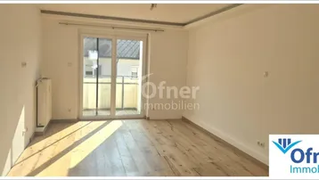 Helles Zimmer mit Holzboden und Zugang zu einem Balkon, ideal als Wohn- oder Schlafbereich.