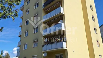 Mehrstöckiges Apartmentgebäude mit gelber Fassade und mehreren Balkonen unter blauem Himmel.