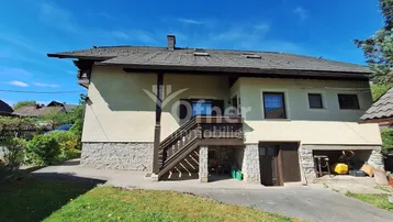 Traditionelles Einfamilienhaus mit Steinsockel, Holztreppe und Satteldach, umgeben von Grünflächen.