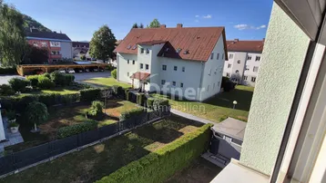 Blick auf ein Wohngebäude mit Garten und umliegender Wohnsiedlung unter blauem Himmel.