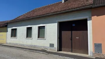 Fassade eines älteren Hauses mit großem Holztor und traditionellem Ziegeldach unter blauem Himmel.