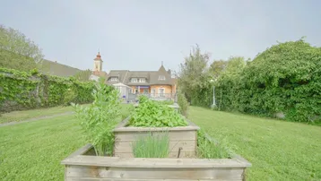 Gepflegter Gartenbereich mit Hochbeeten für den Anbau von Kräutern und Gemüse, im Hintergrund das Wohnhaus.