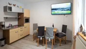 Heller Wohn- und Essbereich mit integrierter Küchenzeile und Wandfernseher.