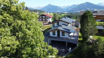 Moderne Häuser in alpiner Landschaft mit Bergblick und viel Grün.