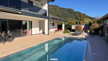 Moderne Villa mit großem Außenpool, weitläufiger Terrasse und herrlichem Bergblick unter blauem Himmel.