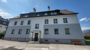 Mehrfamilienhaus mit klassischer Fassade und Satteldach unter blauem Himmel.