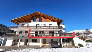 Traditionelles Gebäude mit Holzbalkonen und schneebedeckter Umgebung unter blauem Himmel.