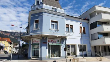 Historisches Gebäude mit hellblauer Fassade, Mansarddach und einem Pizzeria-Geschäft im Erdgeschoss an einer Straßenecke.