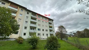 Mehrfamilienhaus mit grüner Umgebung und bewölktem Himmel, Wohnung "Top 14" markiert.