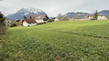Weitläufiges grünes Grundstück mit Blick auf die umliegende Berglandschaft und Wohnhäuser im Hintergrund.